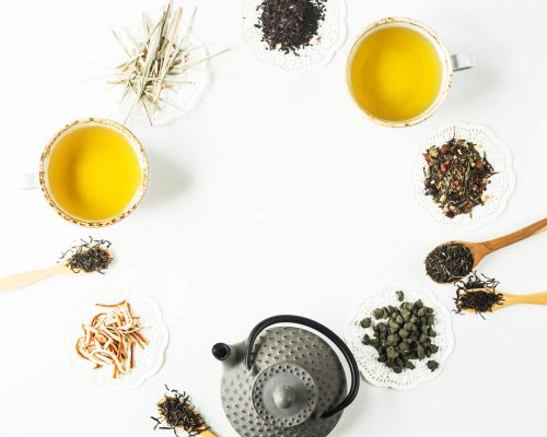 gray-iron-kettle-among-different-kinds-dry-tea-lined-up-circle-cups-with-ready-drink-white-table (1)